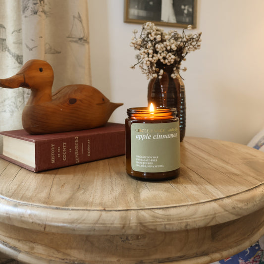 Candle on a wooden table with a wooden duck and books, framed pictures on the wall.