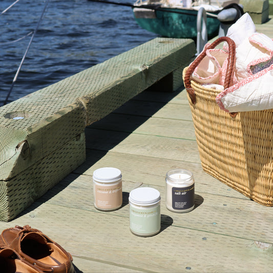 Candles on a wooden dock with a scenic background of water and boats.
